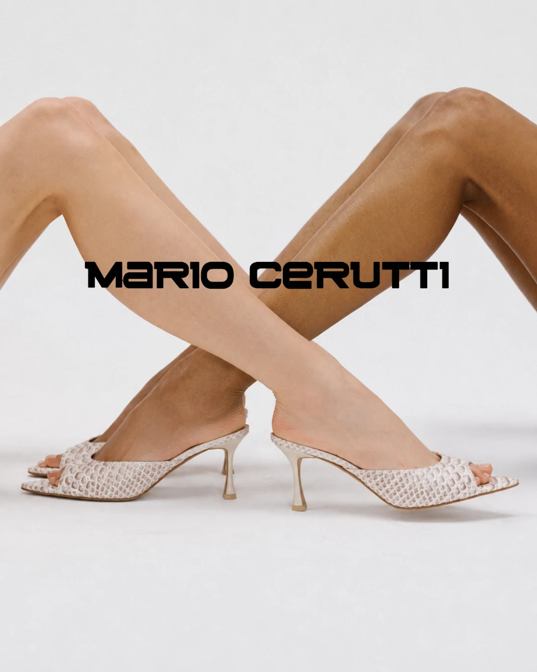 Two crossed legs wearing cream snakeskin Mario Cerutti kitten-heel mules